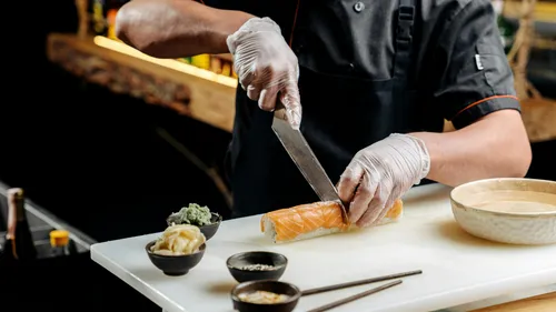 Chef slicing sushi roll on white board.