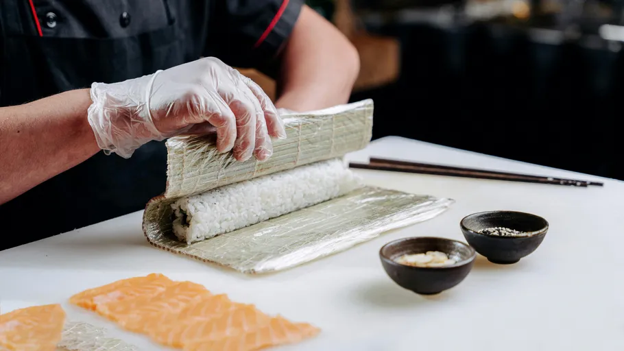 Koch rollt Sushi auf einer Bambusmatte.