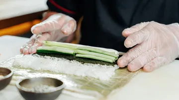 Person rollt Gurkensushi auf Bambusmatte.