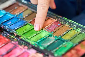 Finger touches green paint in palette.