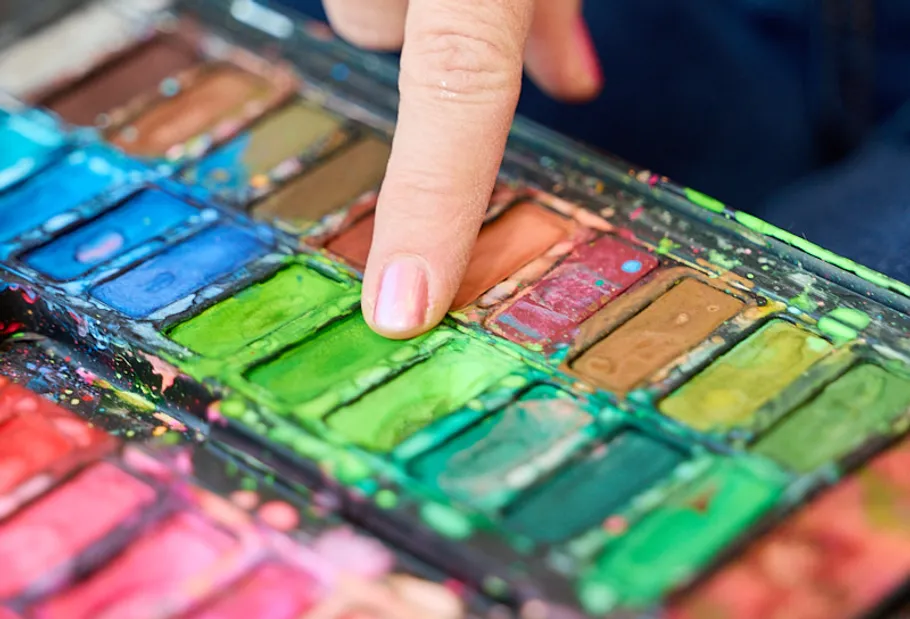 Finger touches green paint in palette.