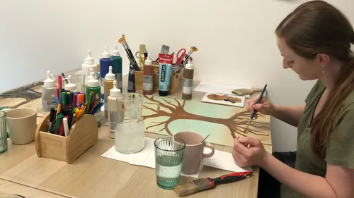 Frau malt Baum an überfülltem Kunsttisch.