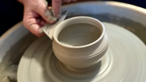 Hand formt Tontopf auf drehender Scheibe.