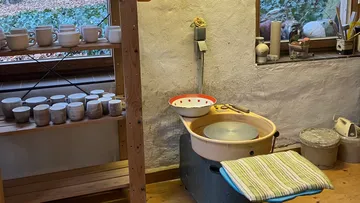 Töpferwerkstatt mit Rad und Regalen voller Tassen.