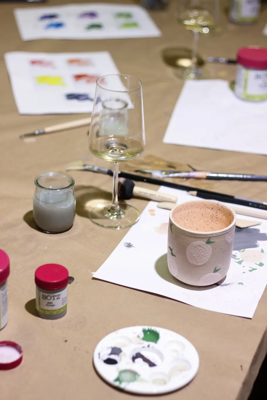 Painting supplies and wine glass on table.