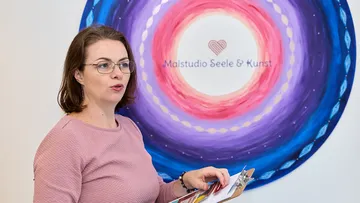 Woman speaks in front of a colorful mural.