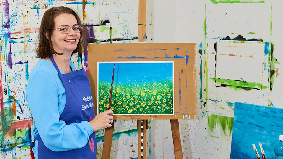 Woman smiling, painting flowers on canvas, colorful studio.