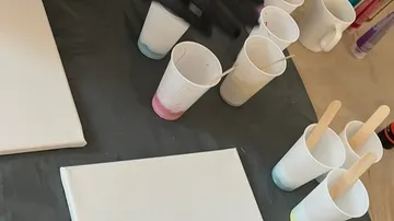 Becher mit Farben, Leinwand, Holzstäbe, Tischaufbau.