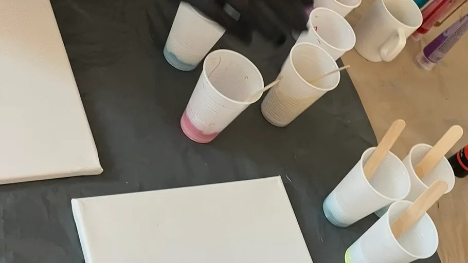 Becher mit Farben, Leinwand, Holzstäbe, Tischaufbau.