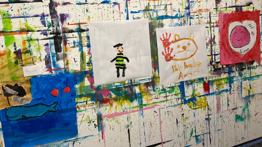 Bunte Kinderzeichnungen an einer bemalten Wand.