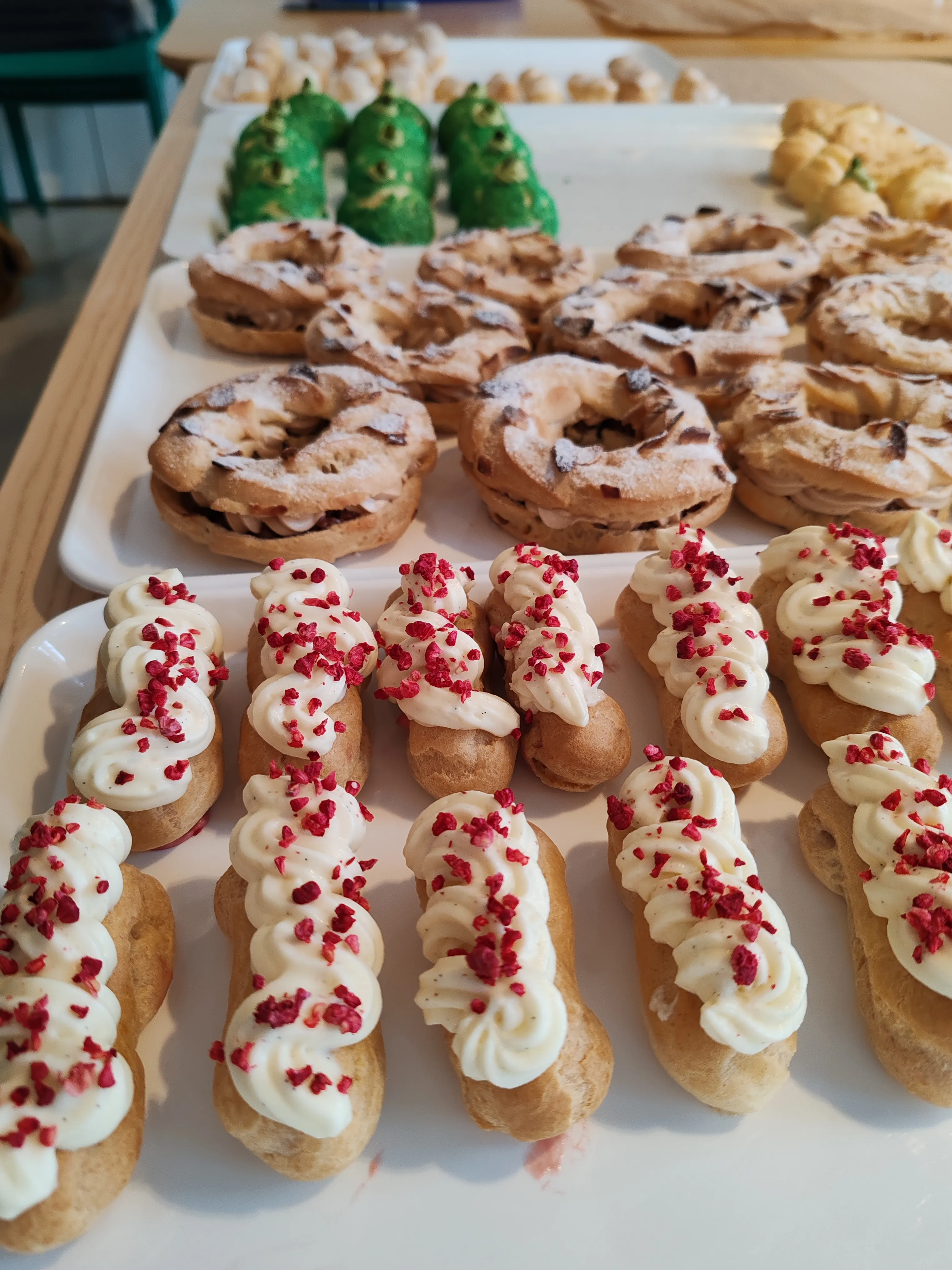 Verschiedene Gebäckstücke mit Creme und Belägen auf Tabletts.