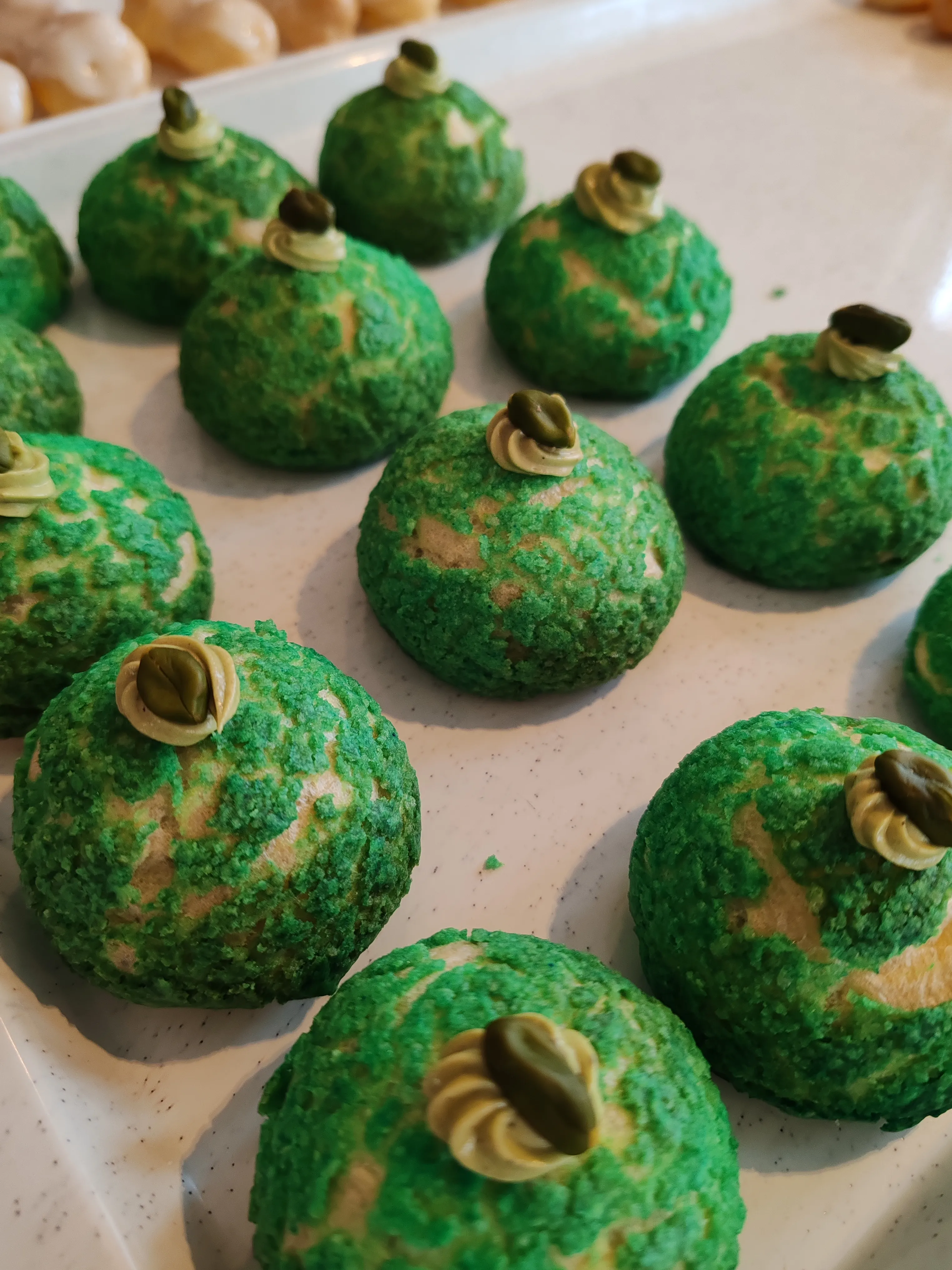 Grüne Gebäckstücke mit Pistazien-Toppings auf Tablett.