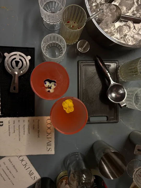Zwei Cocktails mit Blumen auf Bartheke.