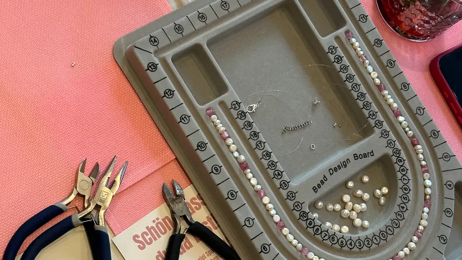 Bead board with tools and pearls on table.