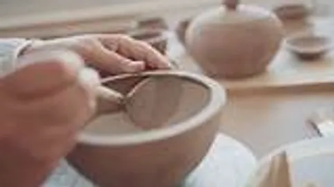 Hands painting ceramic bowl on table.