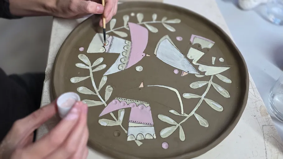 Person painting ceramic plate with colorful design.