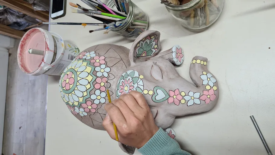Person paints decorative elephant sculpture on table.