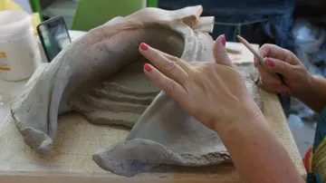 Hands sculpting clay piece on table.