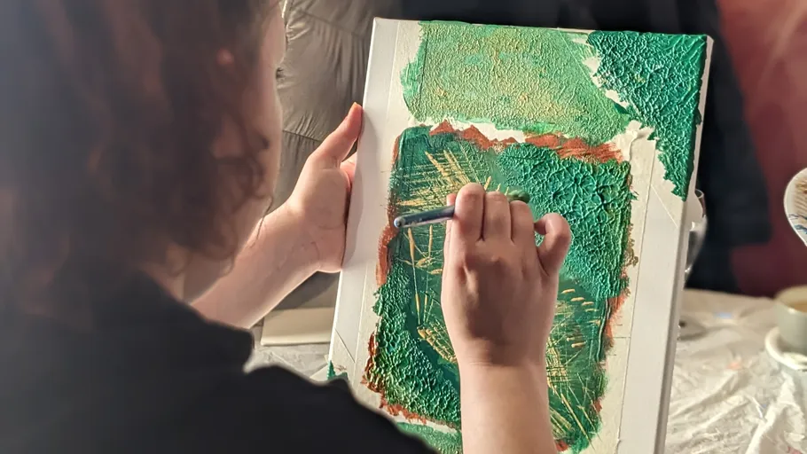 Person painting textured canvas with green paint.