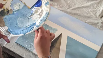 Hands painting with blue on canvas.
