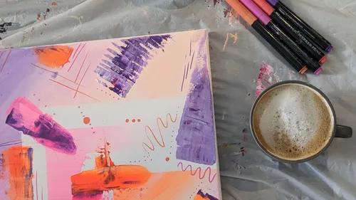 Abstract painting beside coffee and pens.