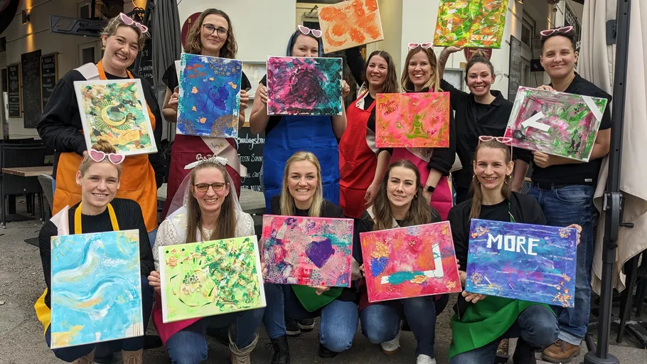 Group of people holding colorful paintings outdoors.