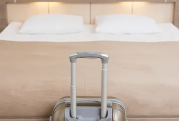 Suitcase in front of neatly made hotel bed.