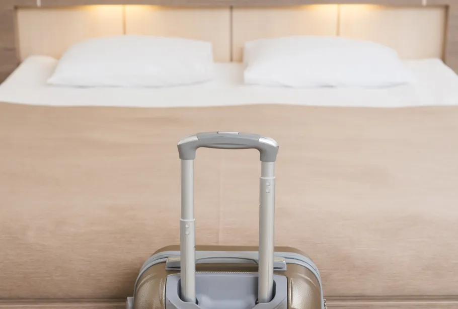 Suitcase in front of neatly made hotel bed.