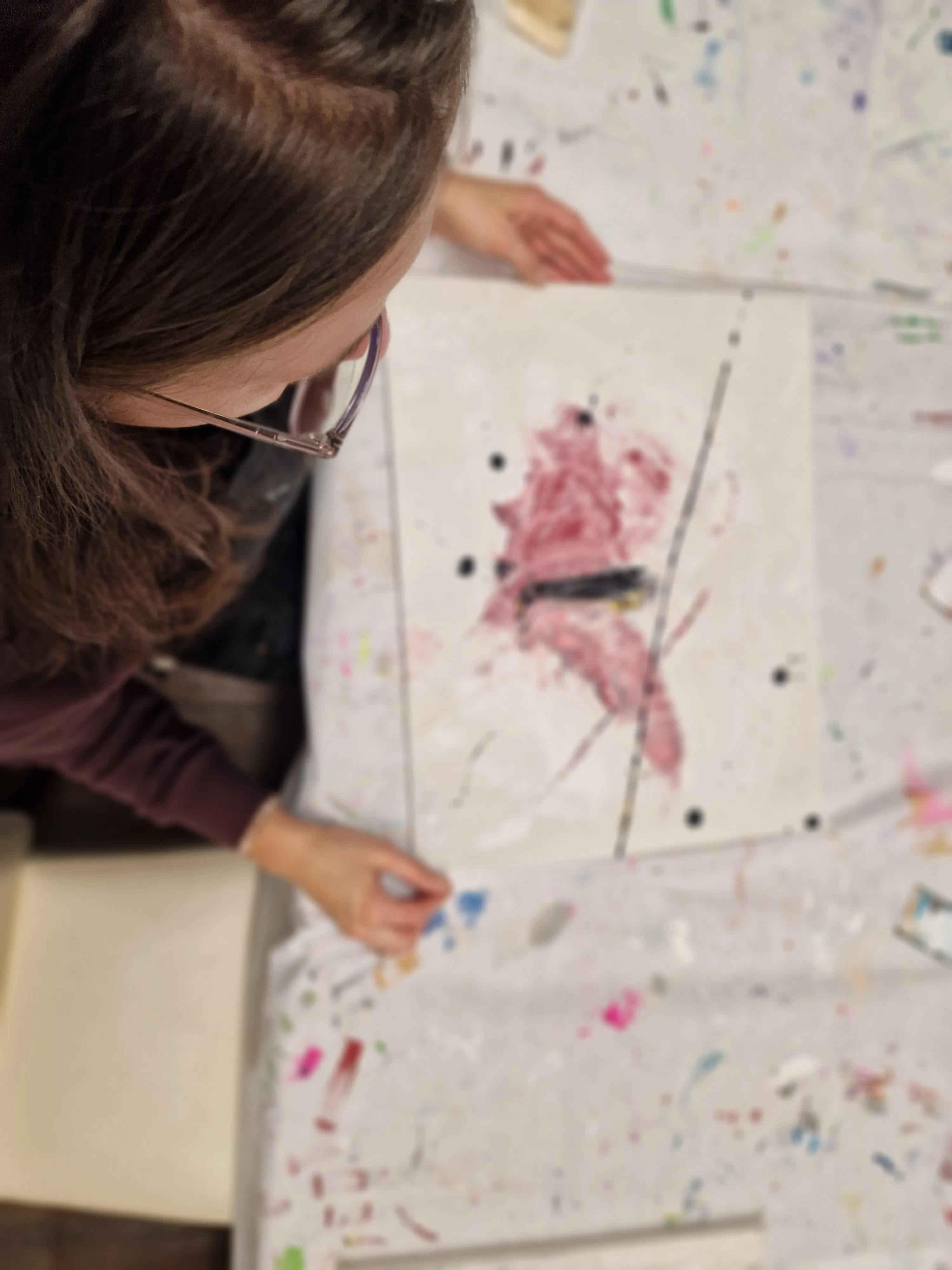 Person malt abstrakte Kunst auf unordentlichem Tisch.