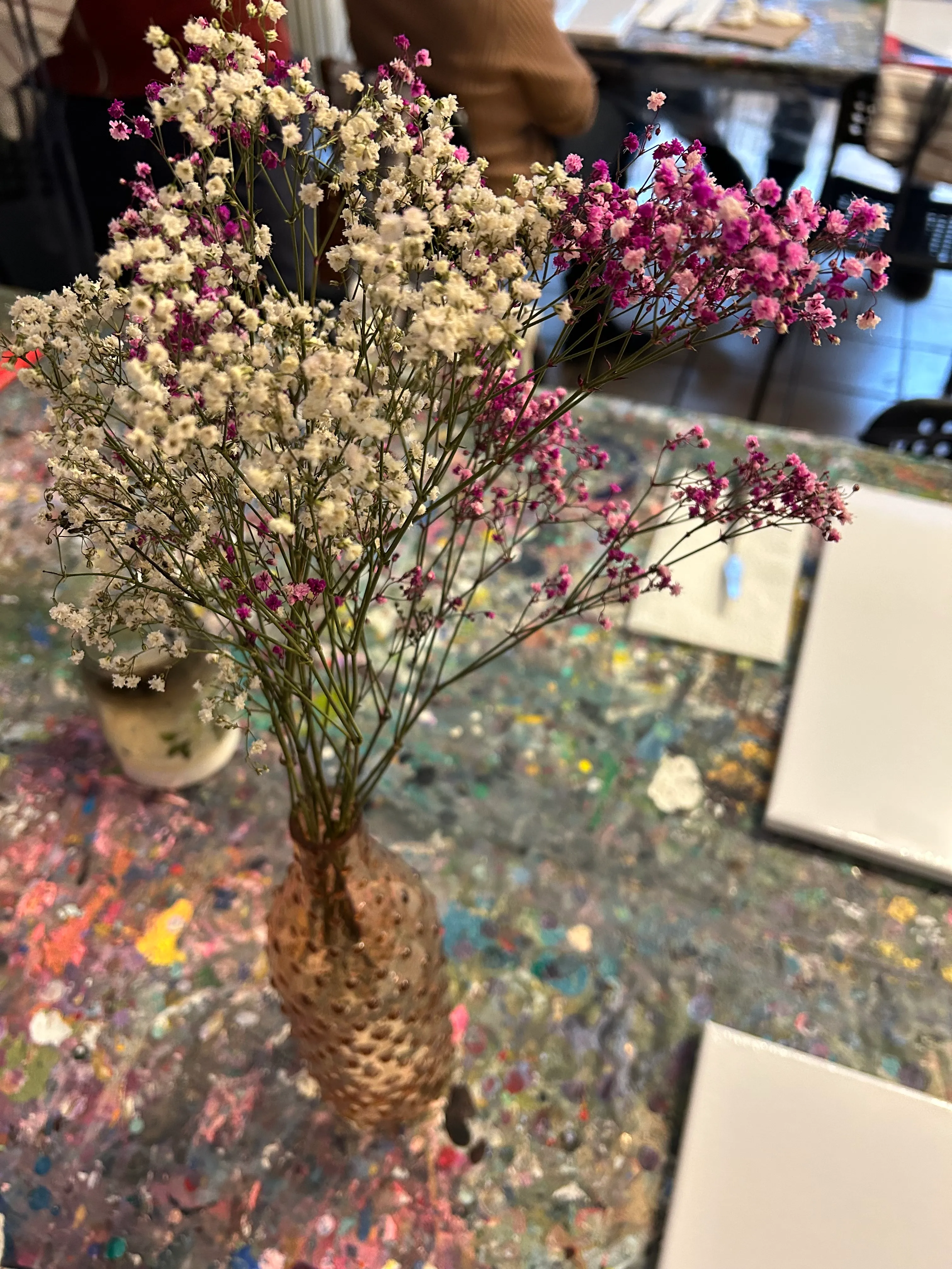 Kleine Blumen in strukturierter Vase auf bemaltem Tisch.