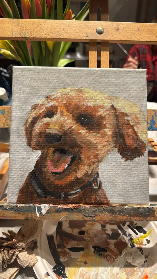 Dog painting on easel with flowers behind.