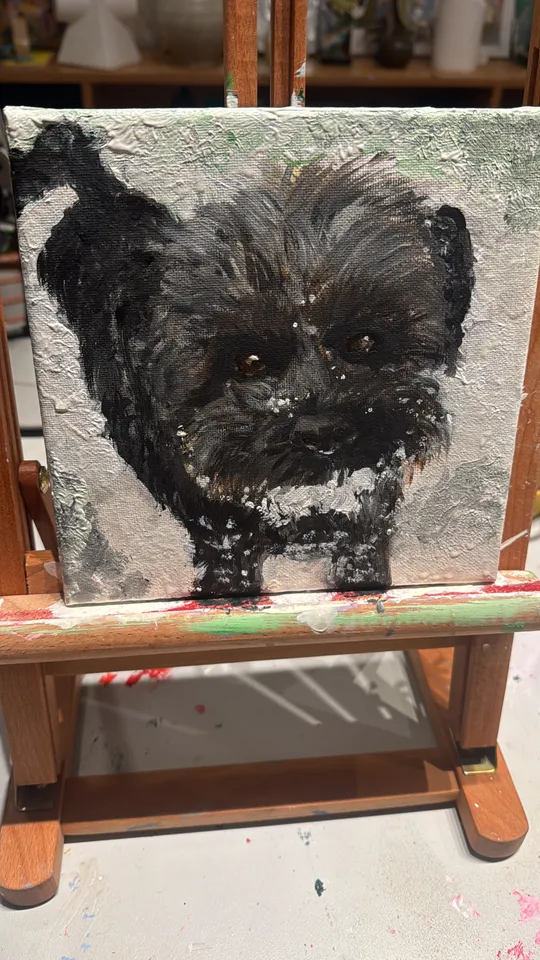 Painting of black dog on wooden easel.