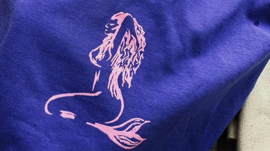 Pinkes Meerjungfrauen-Silhouette auf lila Stoff.