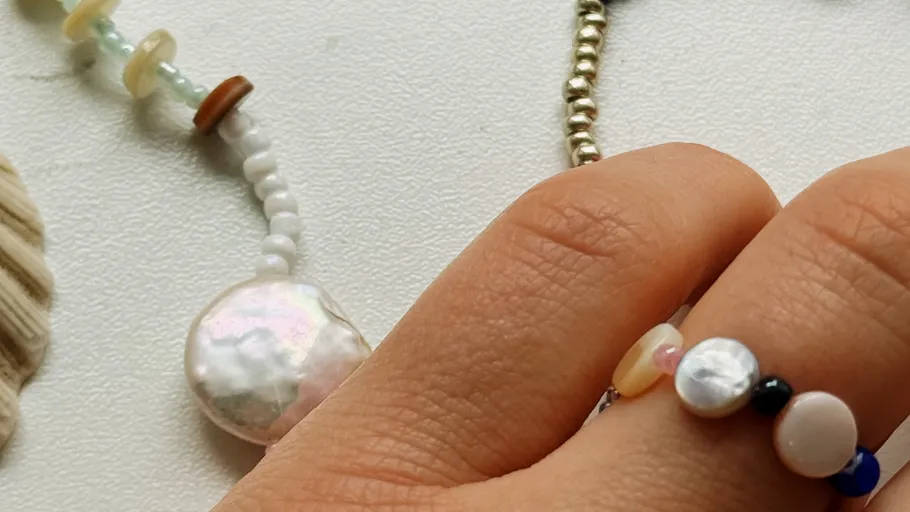 Hand wearing beaded ring on white surface.