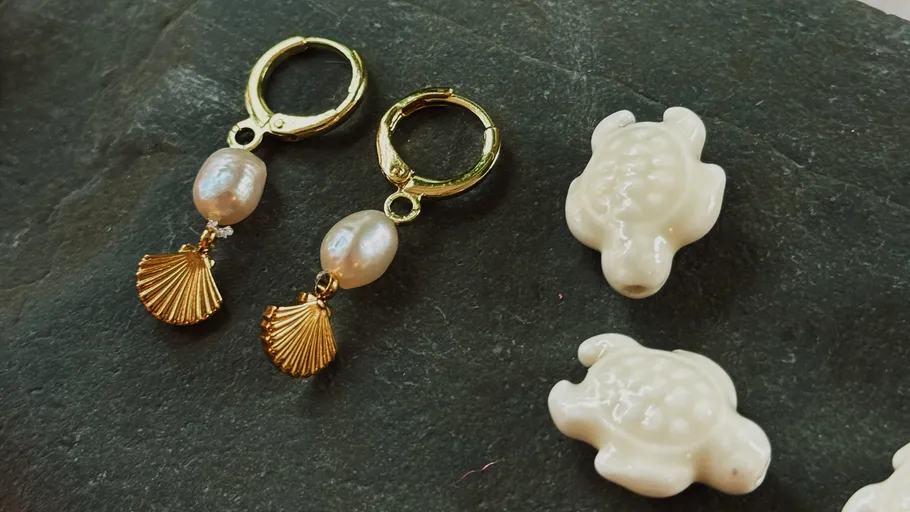 Earrings with pearls and shell charms on slate.