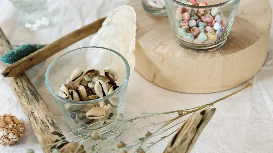Shells and beads in glass cups on table.