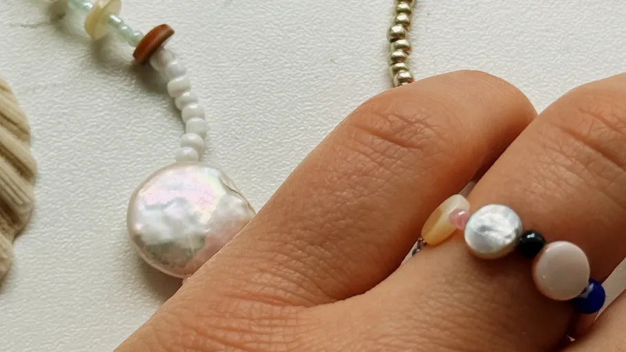 Hand trägt bunten Perlenring, weißer Hintergrund.