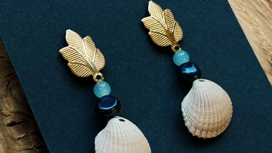 Leaf earrings with shells on dark background.