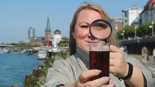 Frau hält Lupe über Getränk am Fluss.