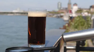 Glass of dark beer on railing by river.