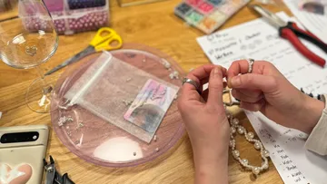 Hands making jewelry at a craft table.