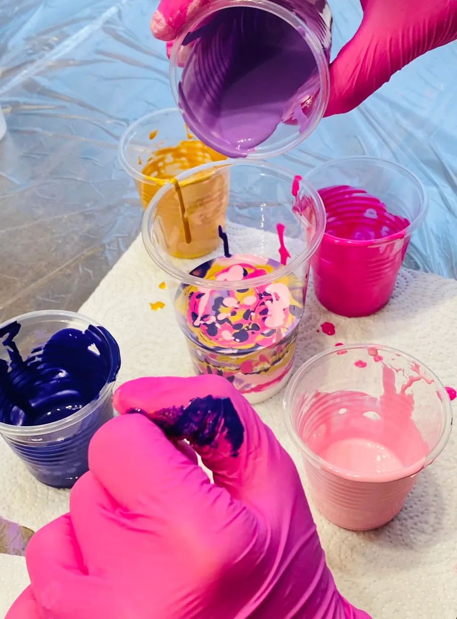Behandschuhte Hände gießen bunte Farbe in Becher.