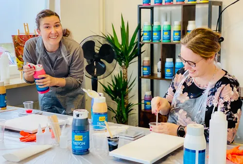 Two women painting in an art studio, smiling.