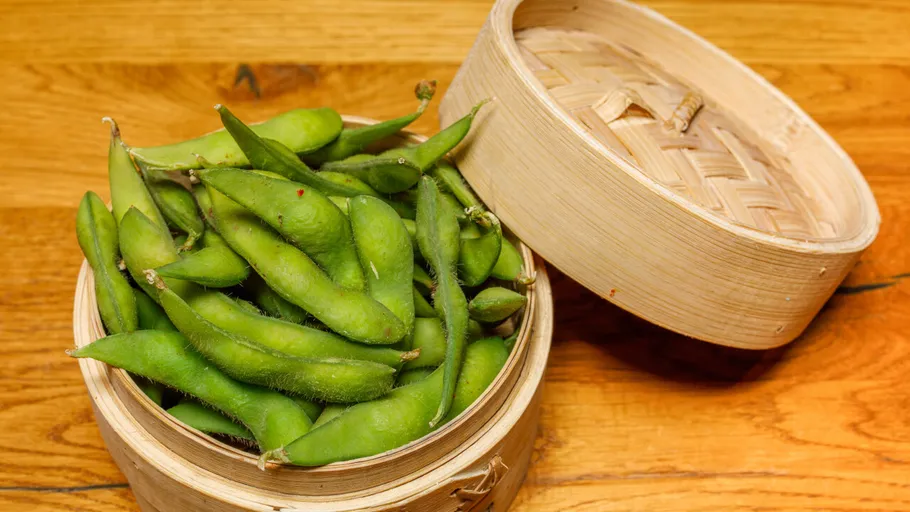 Edamame in Bambusdämpfer auf Tisch.