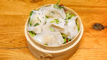 Gedämpfte Teigtaschen im Bambuskorb auf Tisch.