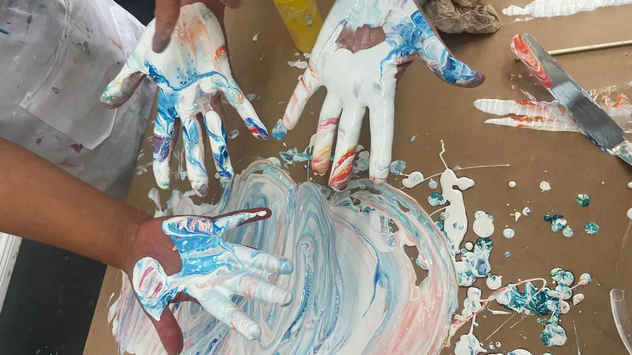 Hands with paint mixing colors on table.