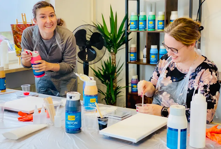 Two women smiling, preparing paint in art studio.