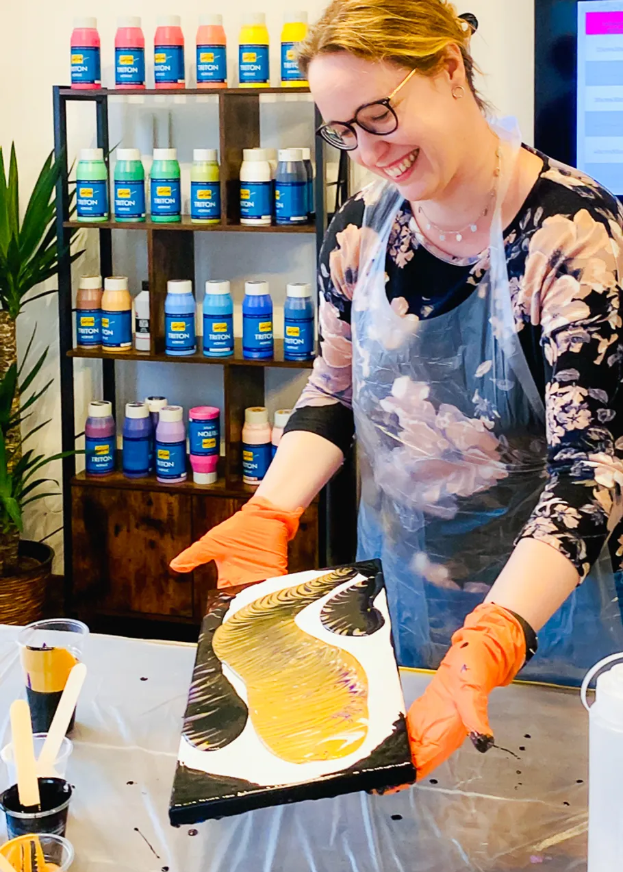 Woman pouring paint on canvas, smiling.