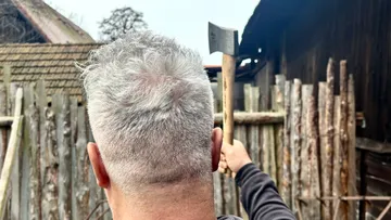 Mann hält Axt vor Holzzaun.