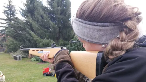 Person zielt mit Gewehr im Garten.